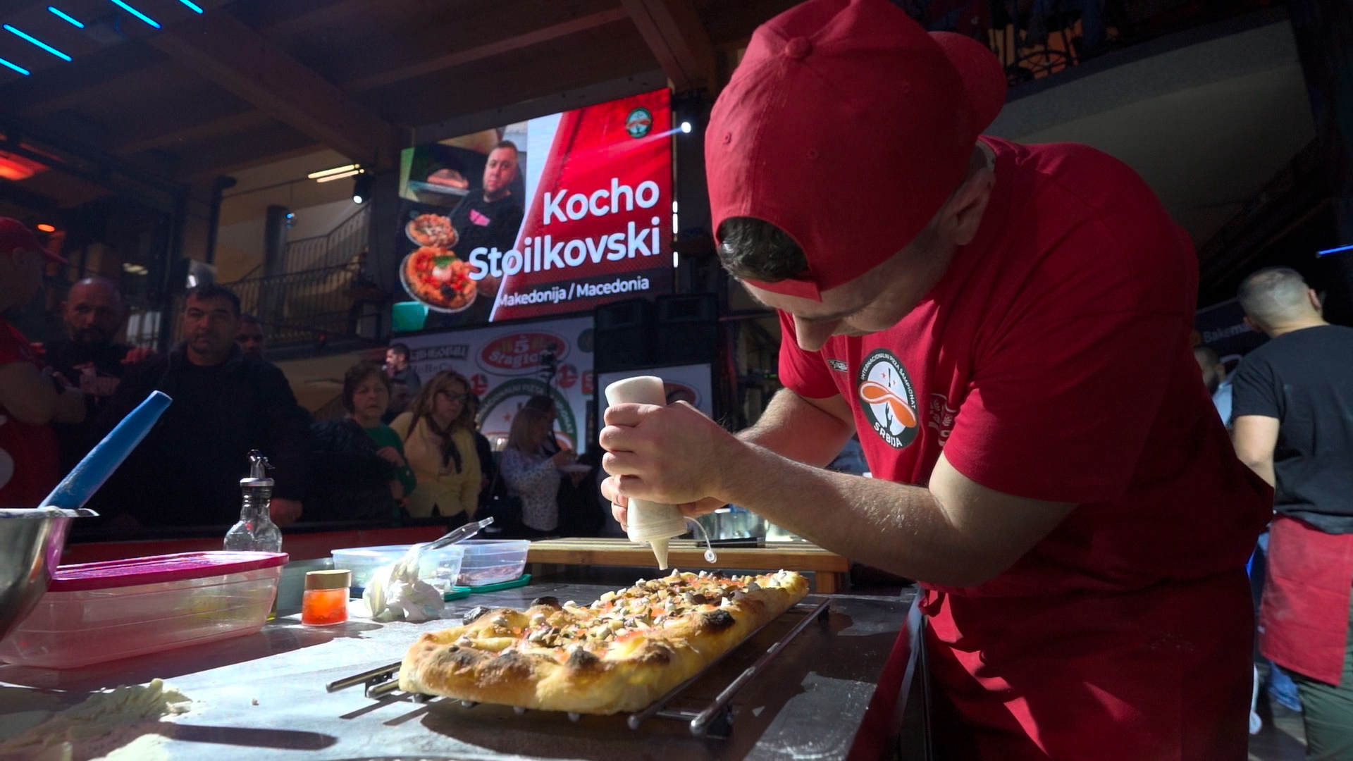a man in an orange shirt making pizzas in a kitchen