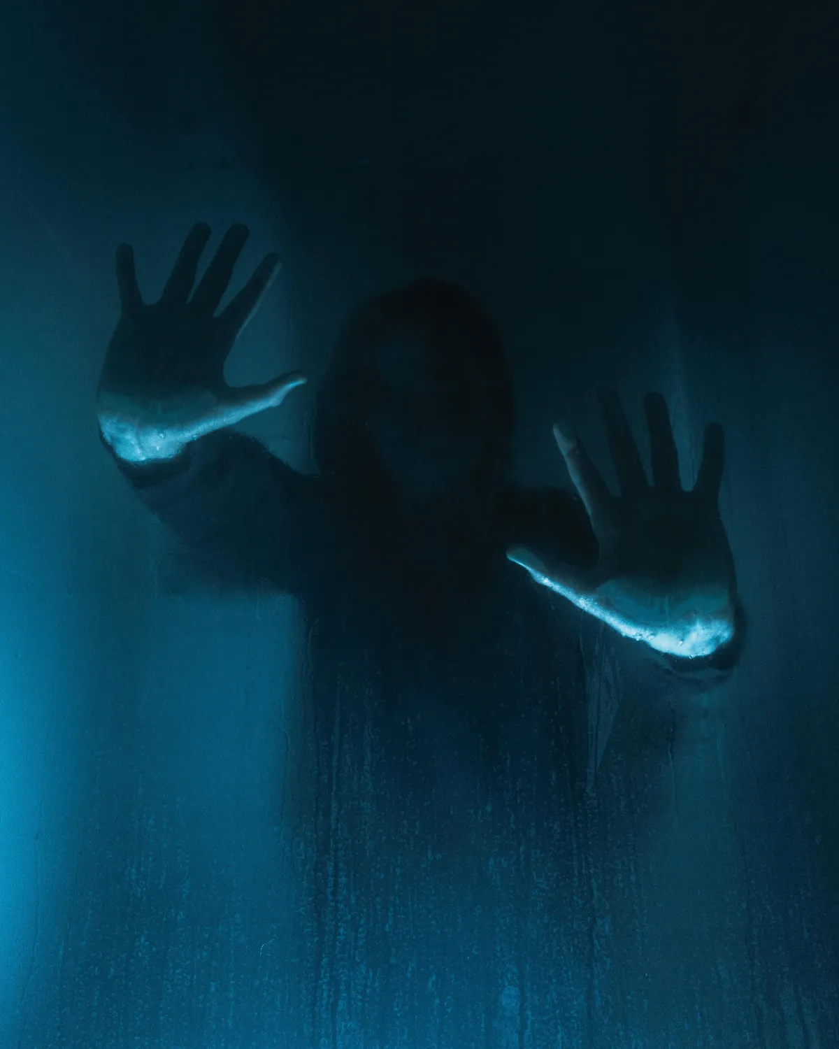 A silhouette of someone with their hands pushed up on a piece of glass that's fogged up.