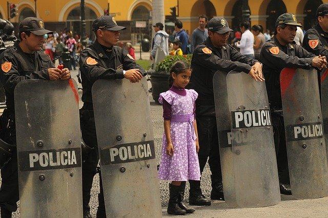 A small girl standing in a row of police armed with riot shields.