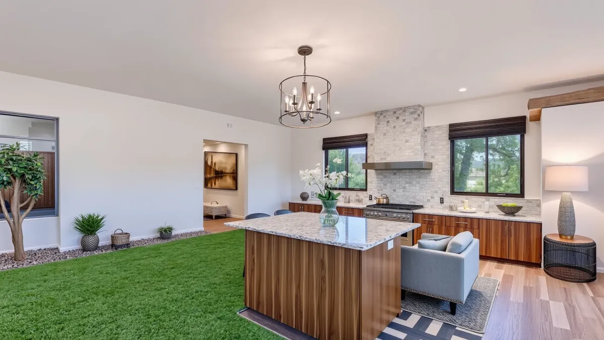 Renovated Floral Park, CA home with modern design, lush lawn, colorful flowers, and a sleek driveway under bright daylight.
