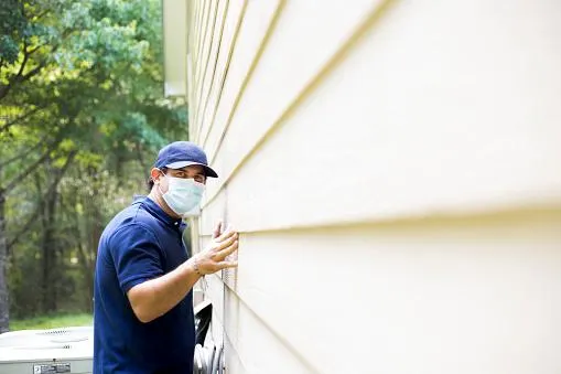 a victoria pest control technician examining the outside wall of a house for pests