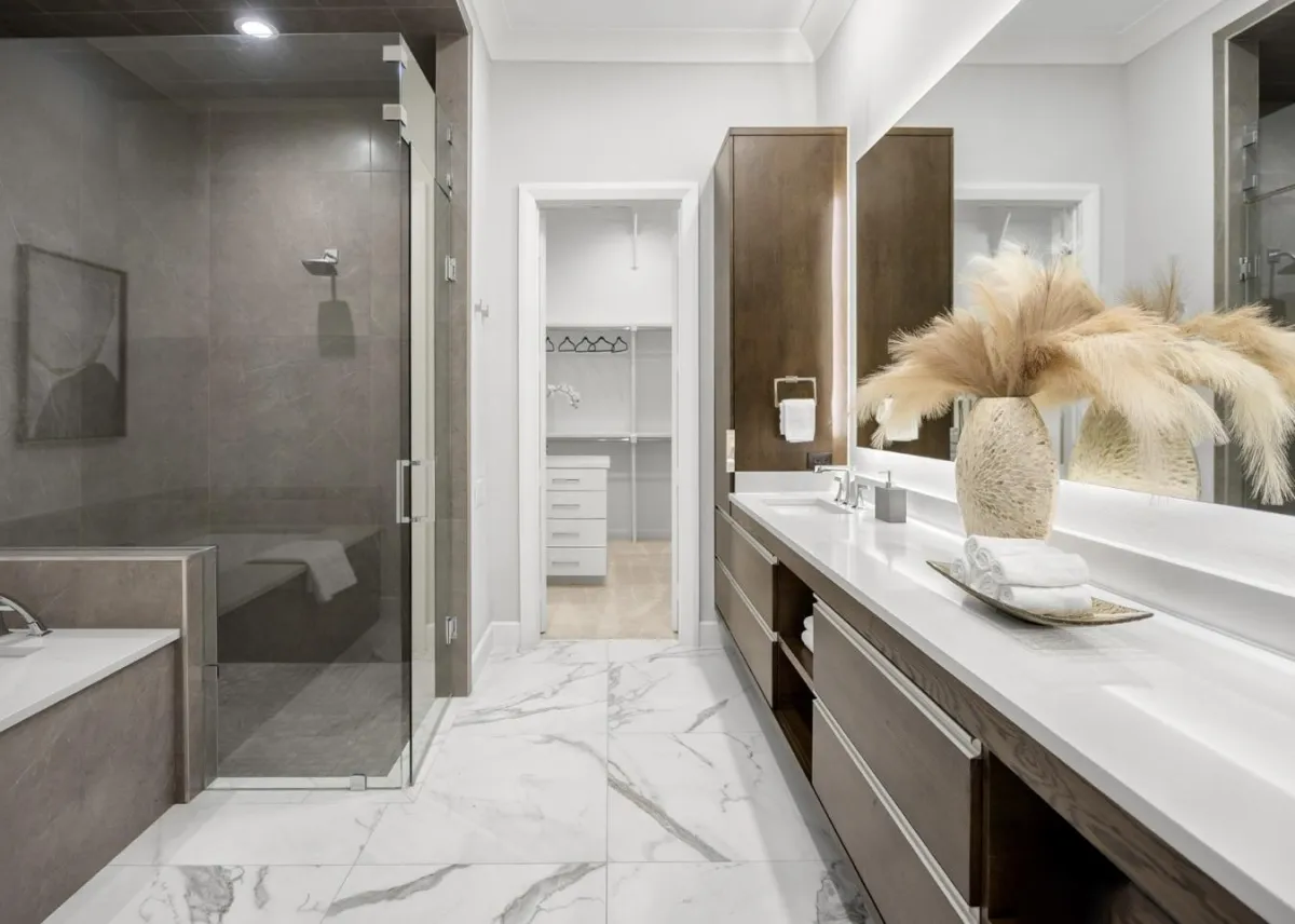 Spacious primary bathroom with dual sinks, a glass-enclosed shower, large soaking tub, and walk-in closet, professionally staged by Model My Home—Dallas Fort Worth home staging and design experts.