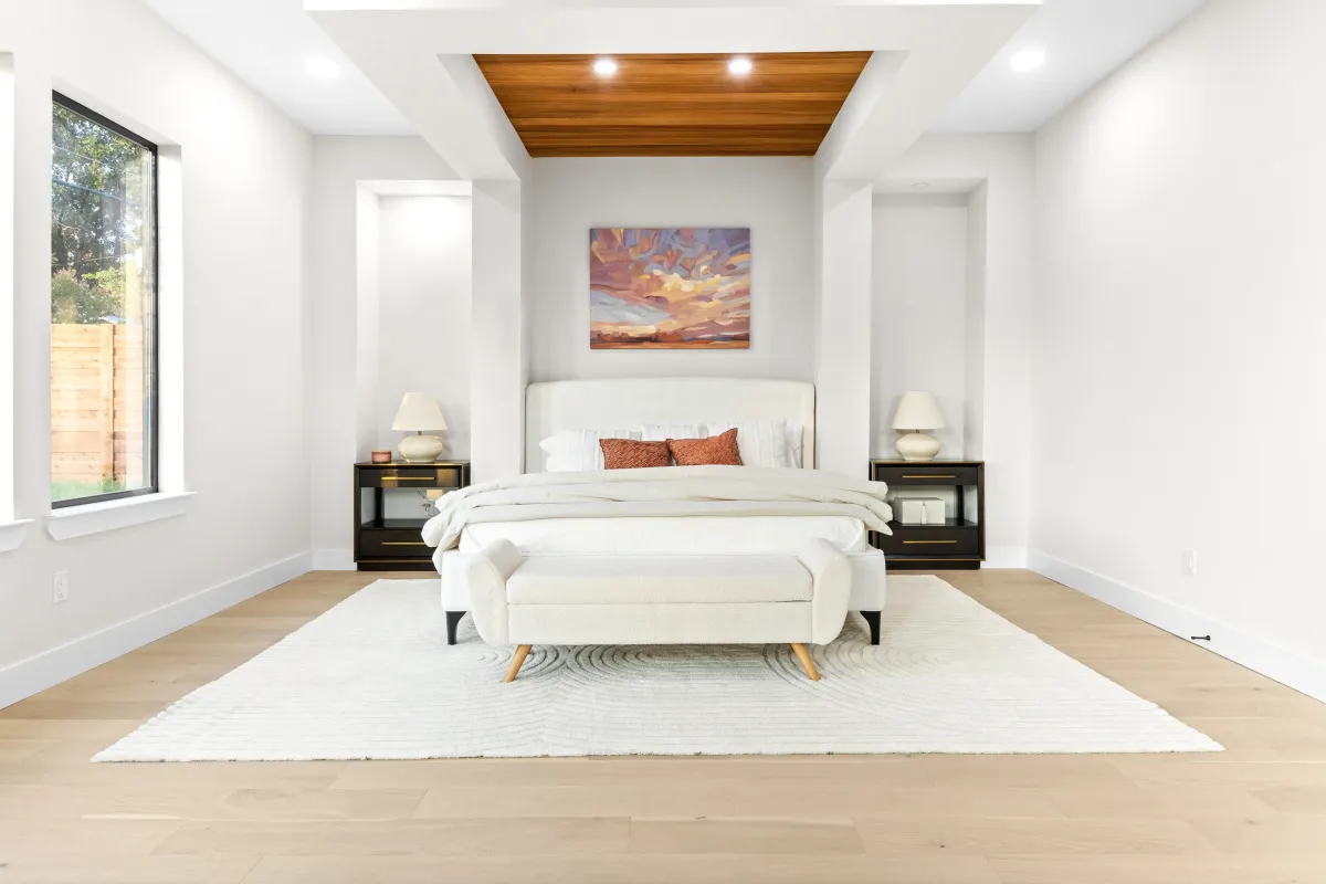 Bright white primary bedroom featuring decorative wall cutouts and a wood panel ceiling accent above the bed, professionally staged by Model My Home—Dallas Fort Worth home staging and interior design experts.