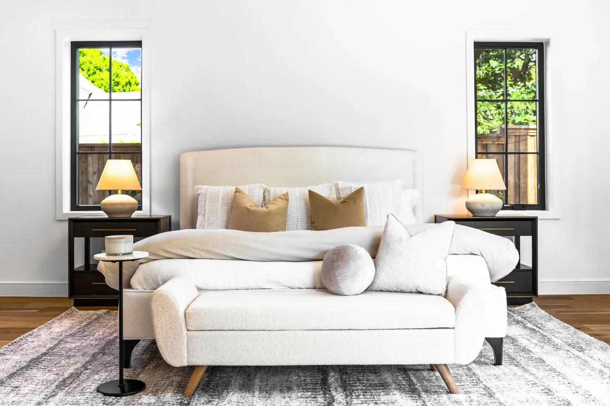 Bright all-white bedroom with a cozy sitting area at the end of the bed, professionally staged by Model My Home—Dallas Fort Worth home staging and interior design experts.