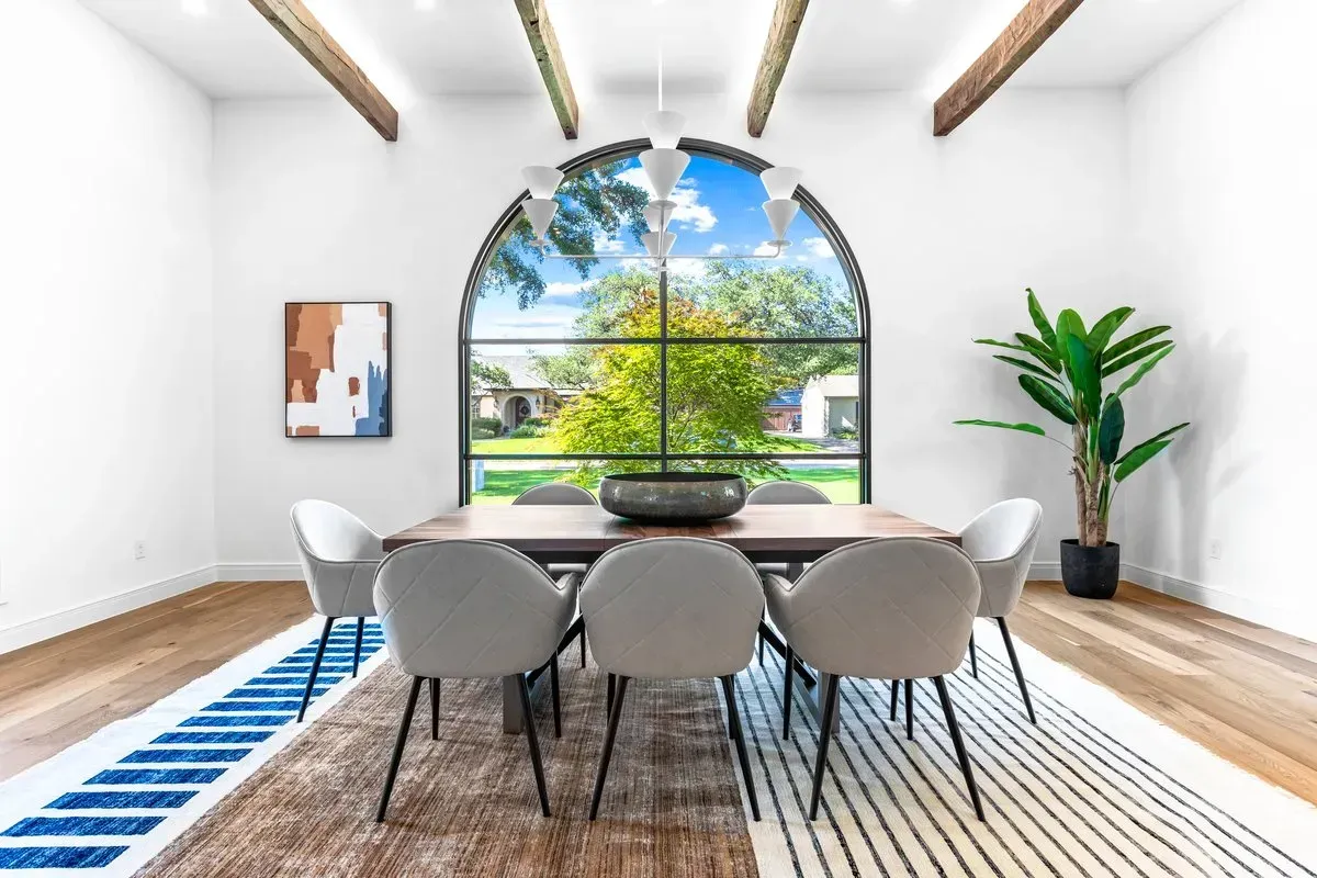 Spacious dining room with exposed ceiling beams, a large arched window, and room for an eight-person table, professionally staged by Model My Home—Dallas Fort Worth home staging and design experts.