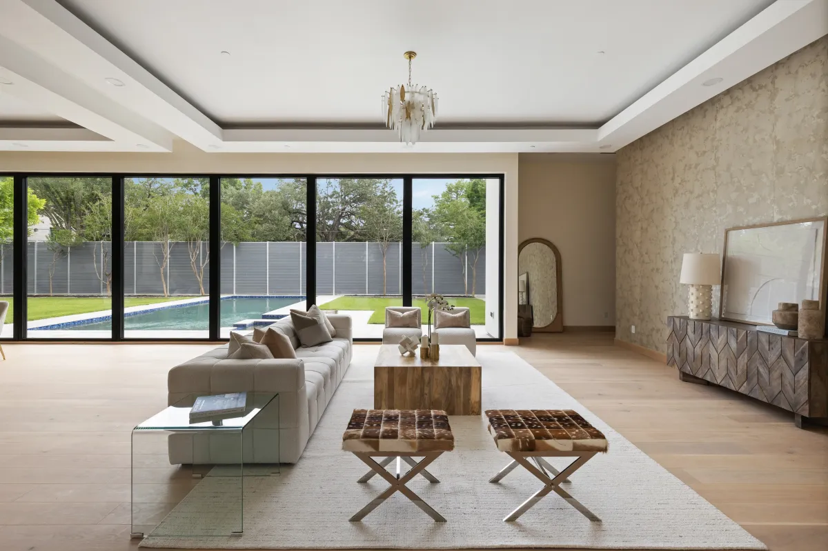 High-end luxury staged living room with an open-concept design and a full wall of doors opening to a backyard pool, creating an elegant indoor-outdoor living experience—professionally styled by Model My Home, Dallas Fort Worth home staging experts.