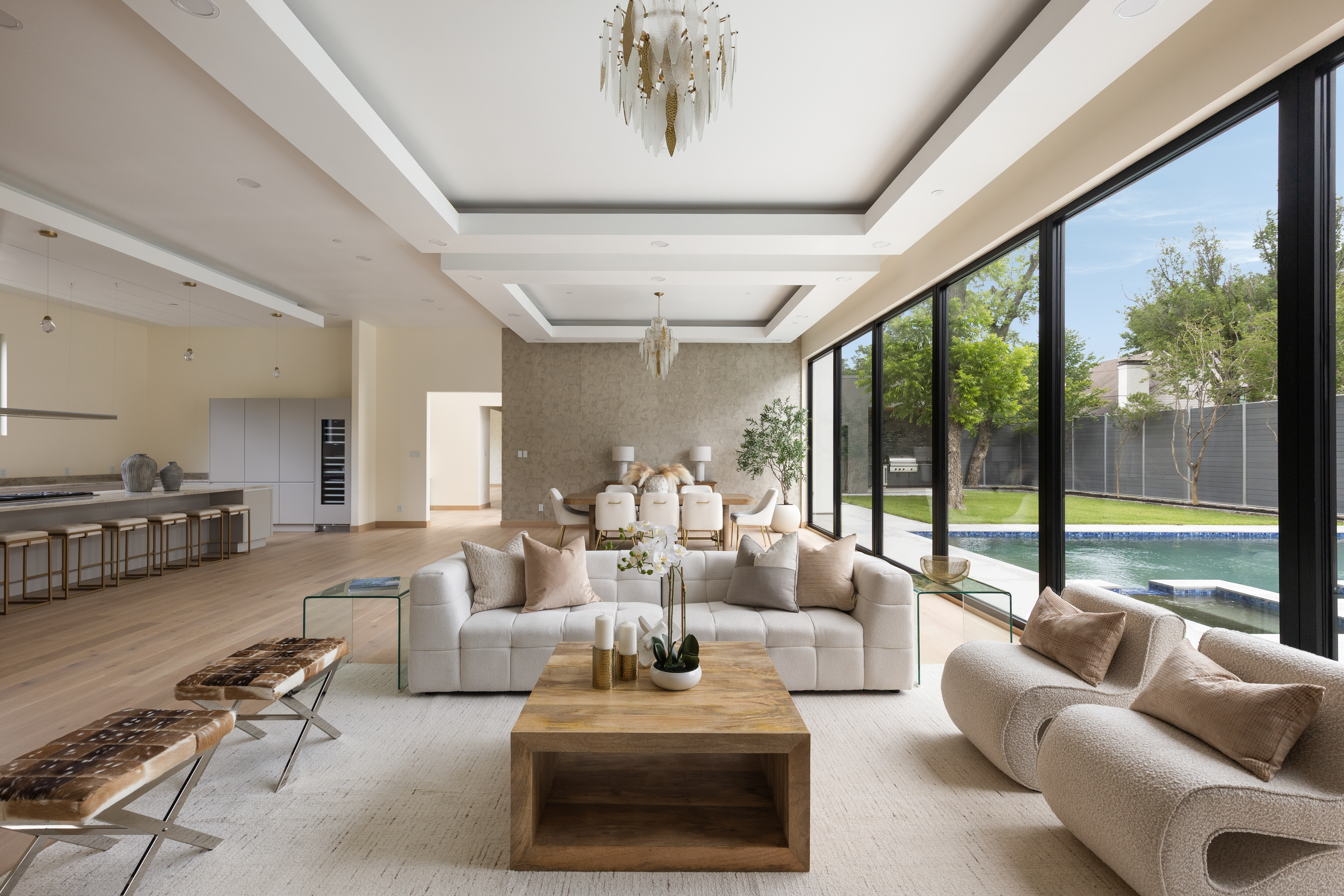 Spacious luxury living room with a full wall of floor-to-ceiling glass doors opening to a backyard with a large pool, professionally staged by Model My Home—Dallas Fort Worth home staging and design experts.