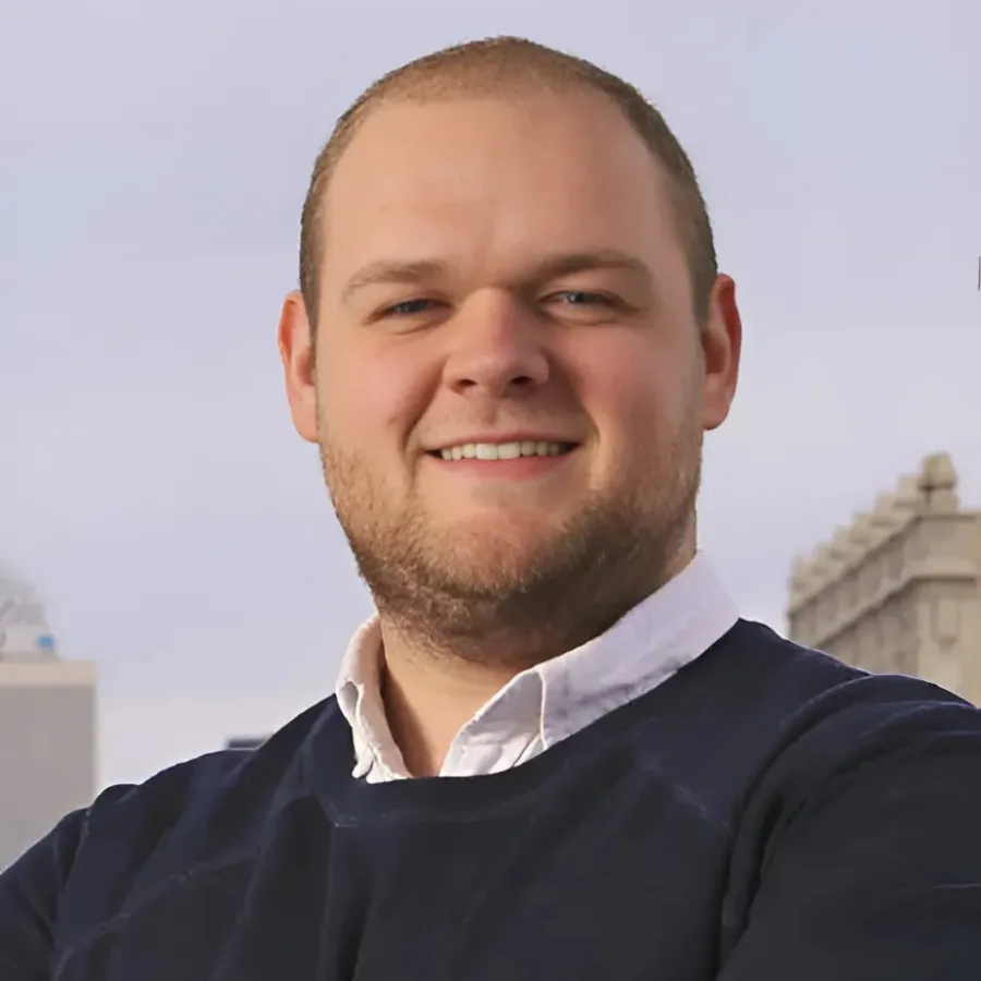 Confident young professional man outdoors, smiling with arms crossed, city skyline in background