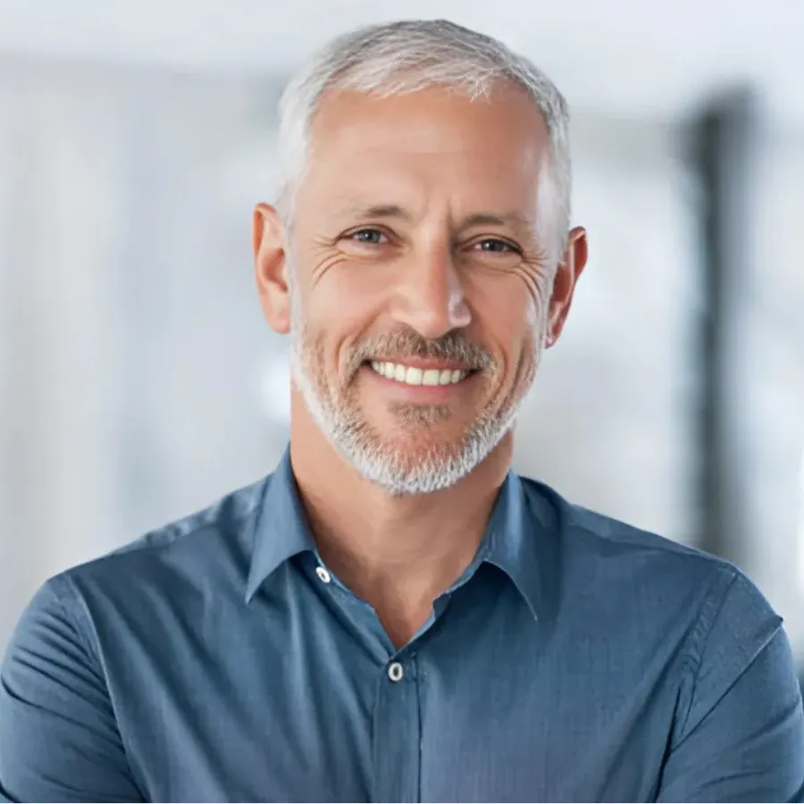 Mature man with salt-and-pepper hair smiling in modern office setting, arms crossed