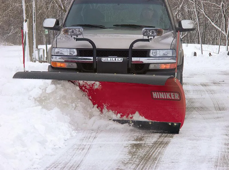 Red pickup truck with BOSS DXT snow plow clearing heavy snow on a forest road during winter