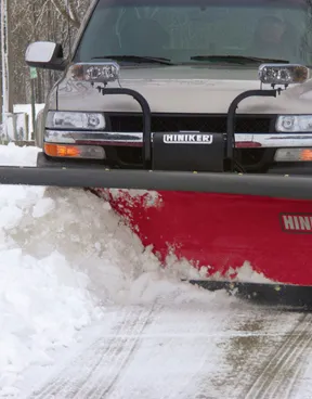 Red pickup truck equipped with BOSS DXT snow plow clearing heavy snow from a winter road