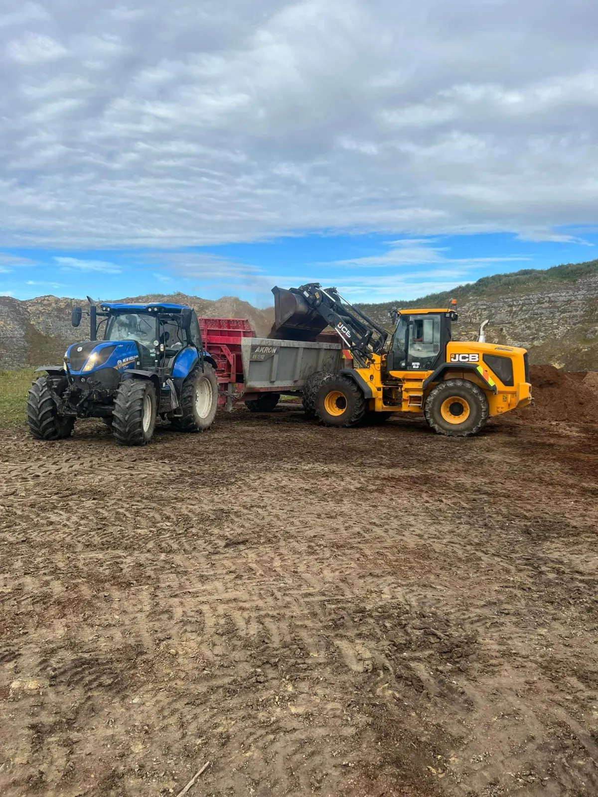 Yellow digger loading soil into red tip trailer attached to blue tractor during farm excavation work in Southland