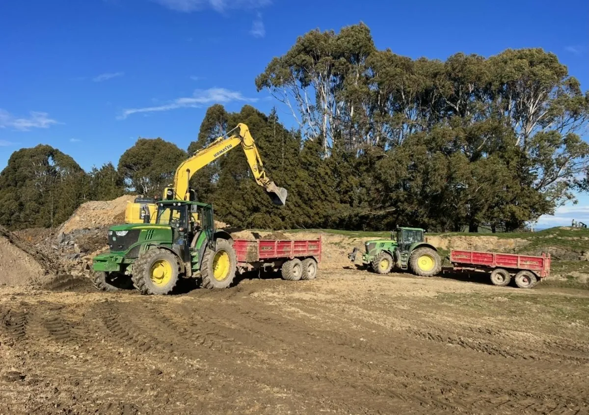 Excavator loading a yellow trailer during site excavation near tree line