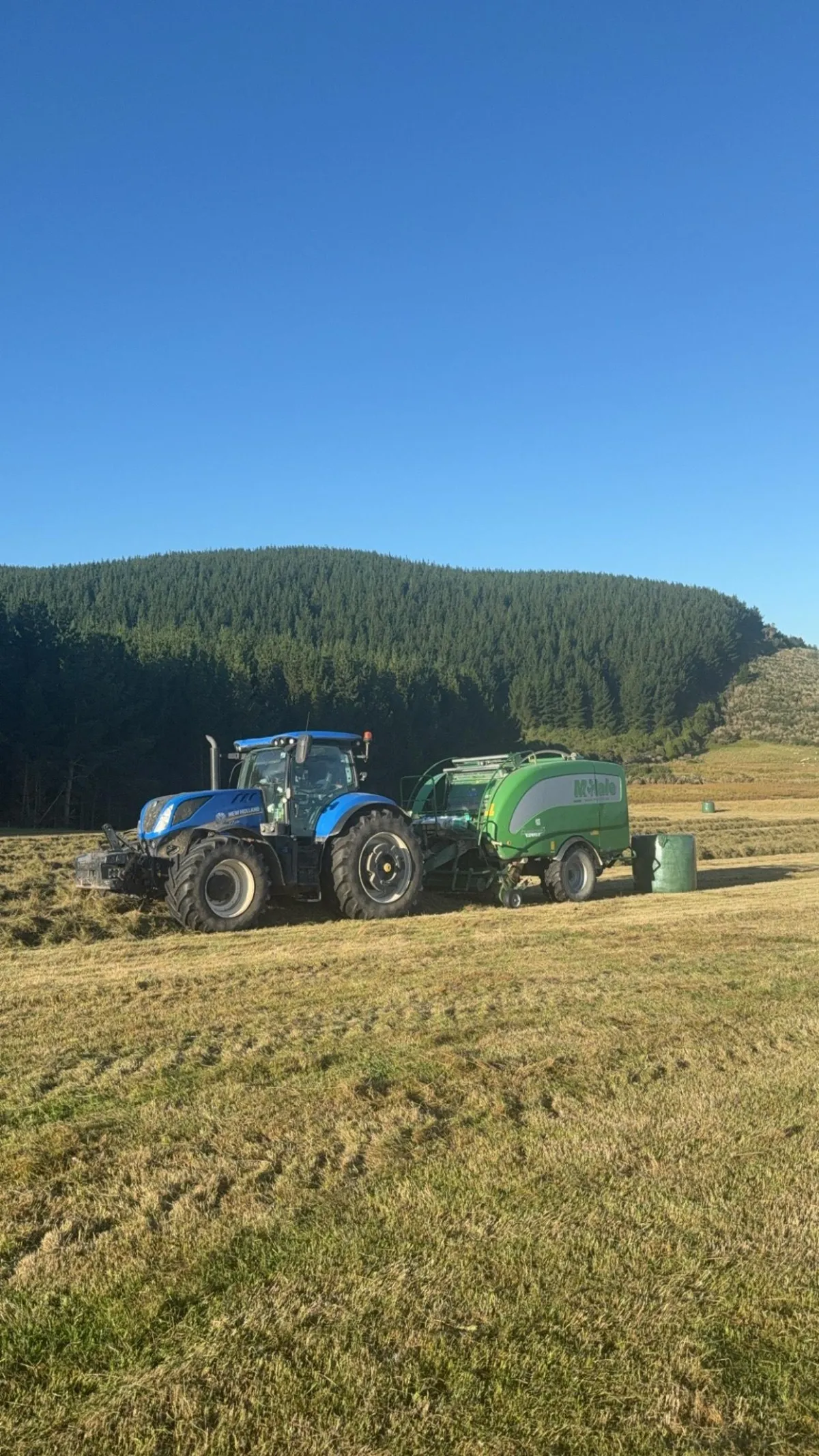 Tractors applying fertiliser or spray in an open field near pine shelterbelt