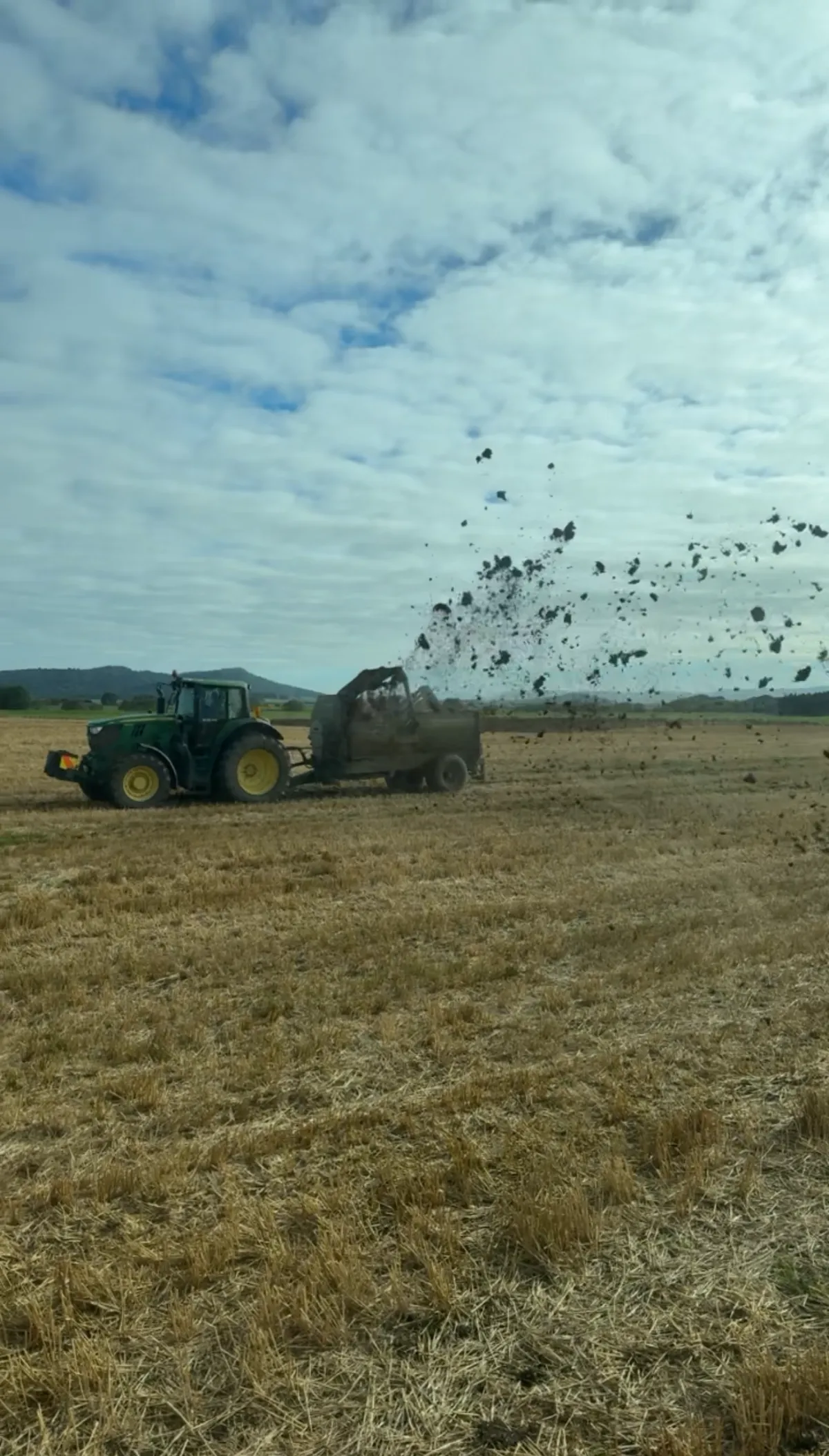 Tractor spreading manure across a dry paddock during a muck spreading job in Southland, New Zealand