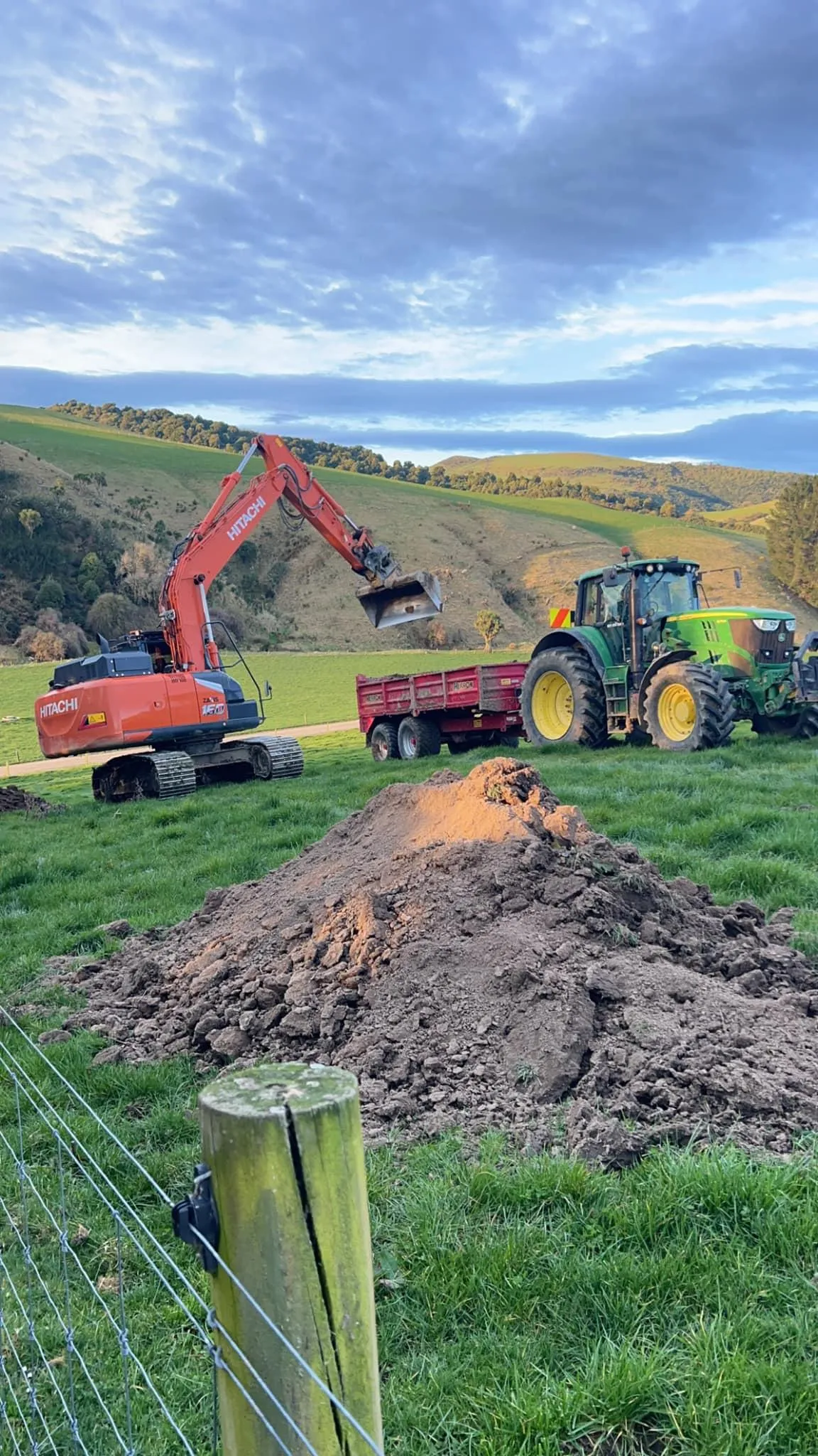 Excavator and tractor completing a dirt mound project on a rural farm