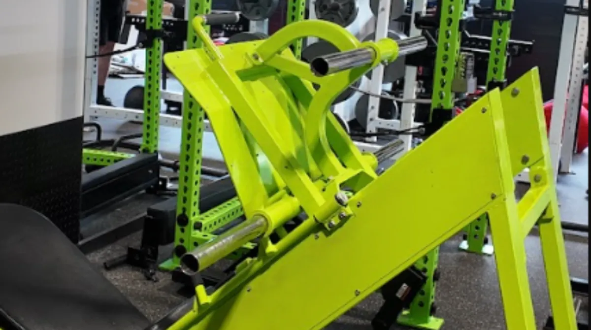A custom-painted toxic green plate-loaded leg press machine with an extra-wide footplate standing on an industrial rubber floor in front of heavy power racks at a strength facility serving Southbury, CT.