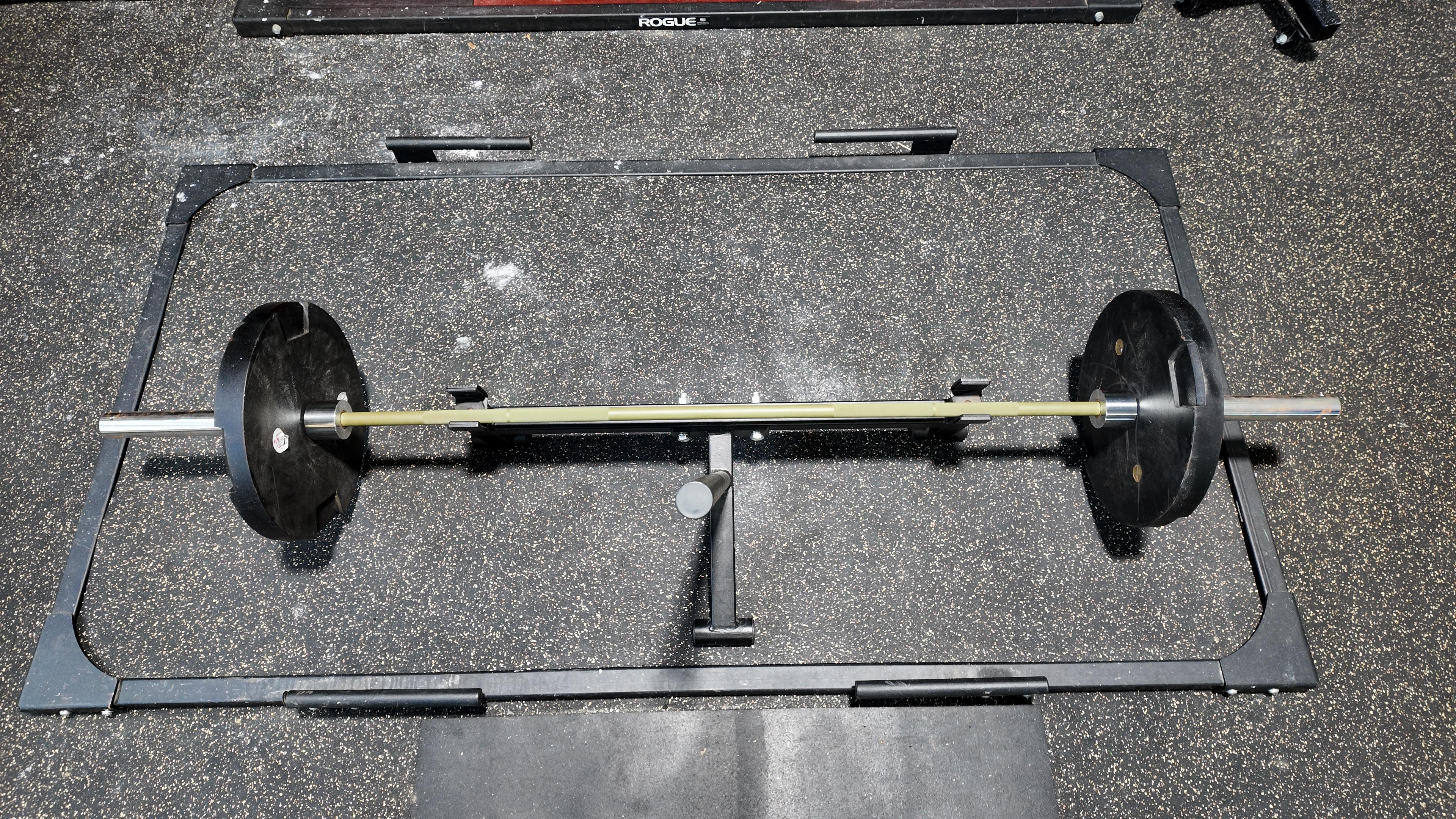 An overhead, top-down view of a loaded powerlifting barbell resting on a specialized deadlift platform frame with industrial rubber flooring at The Strength Lab in Newtown, Connecticut.