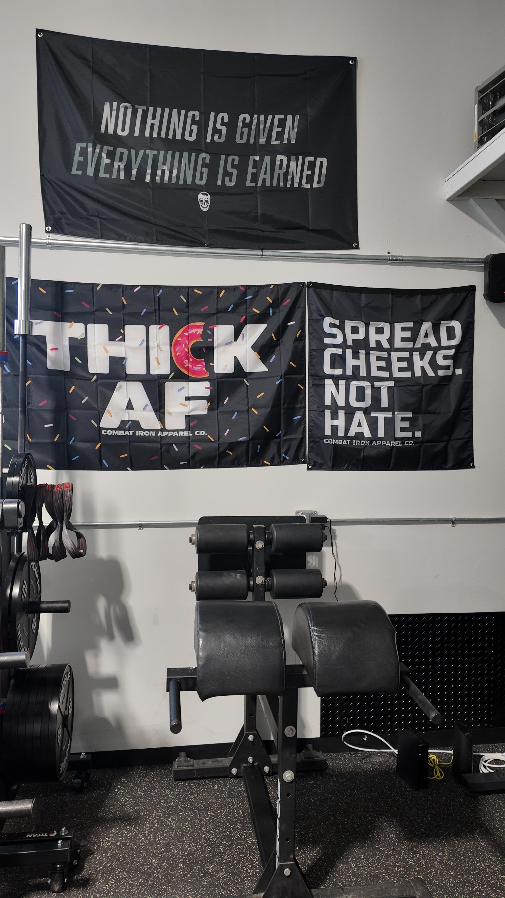 A professional black Glute Ham Developer (GHD) machine on a rubber gym floor inside The Strength Lab powerlifting facility in Newtown, Connecticut. The white wall in the background displays motivational strength culture banners, alongside a vertical barbell and weight plates.