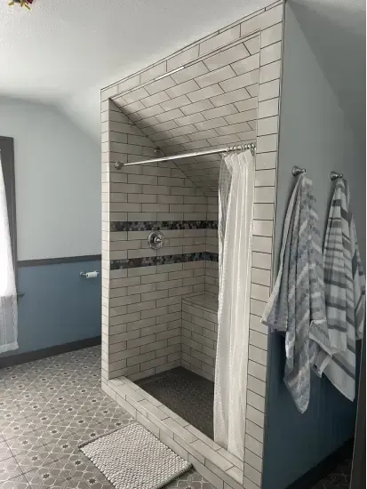 A custom walk-in shower in an attic space with a sloped ceiling shower with grayish tile in the ceiling of the shower.