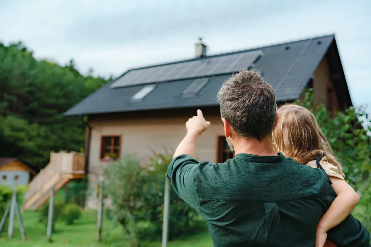 Dad holding daughter pointing at their home that has solar panels on the roof top
