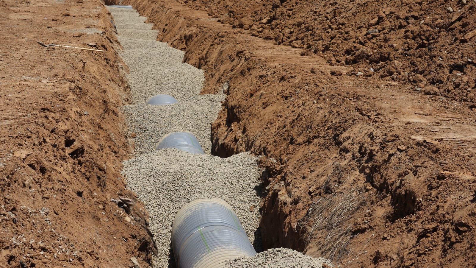 Open utility trench in red clay soil with pipe bedded in gravel