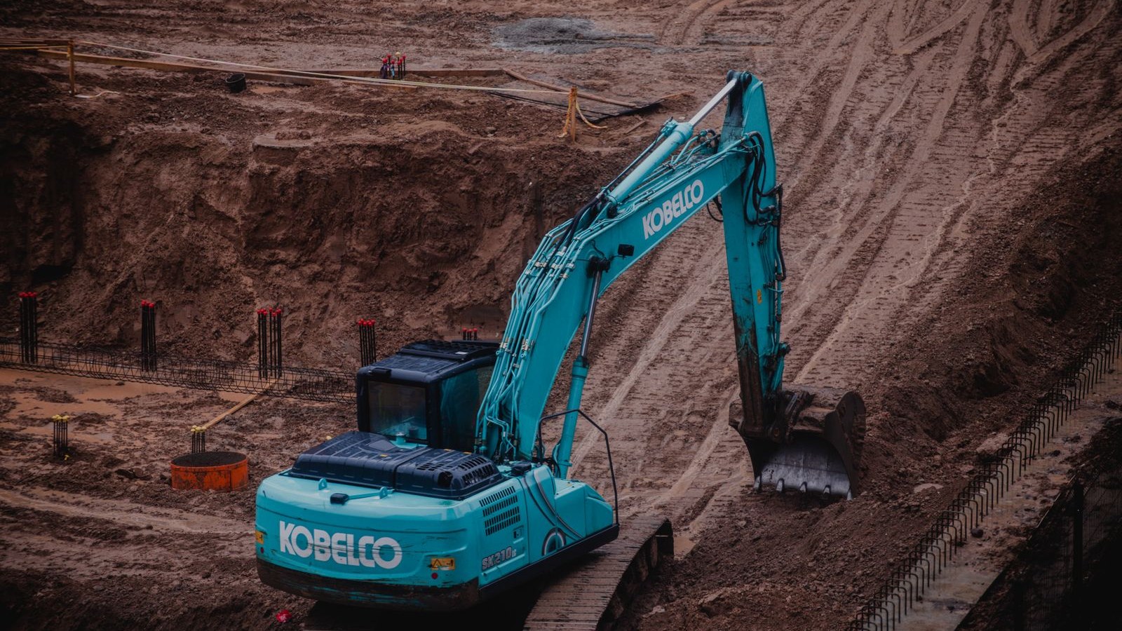 Excavator digging a foundation pit with rebar piers at a construction site