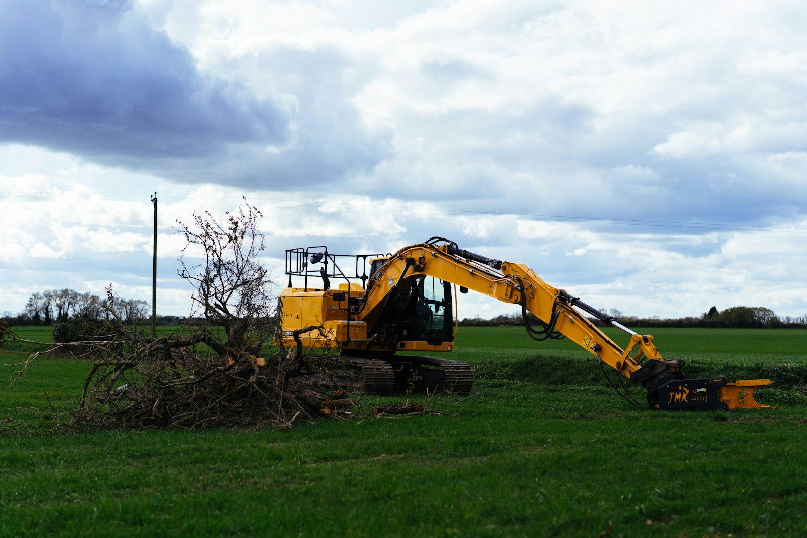 Excavator beside a pile of cut brush and tree limbs on a cleared Middle Tennessee field