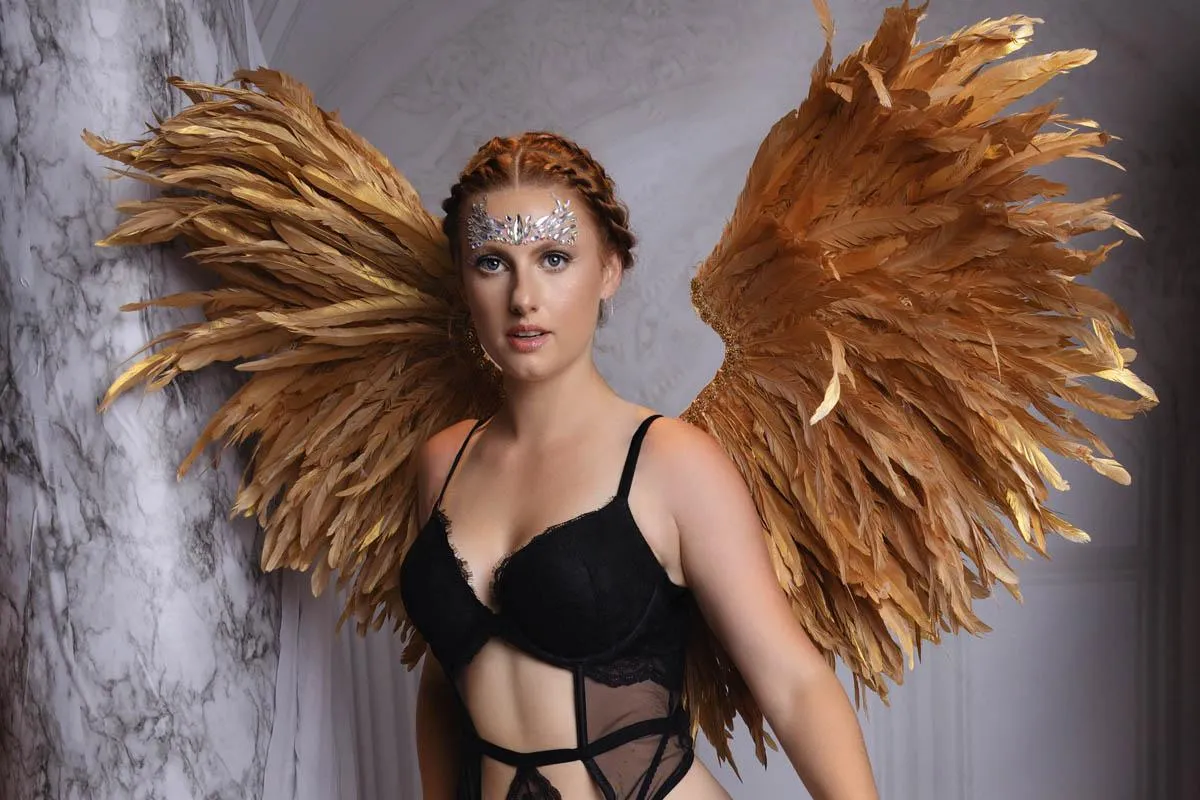 A woman in black lingerie with golden wings poses for a boudoir shoot in Indianapolis at Enchanted Moments Artistry.