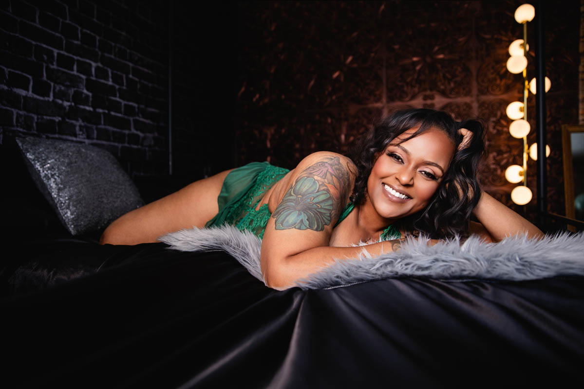 Woman smiling on bed during boudoir session with warm lighting