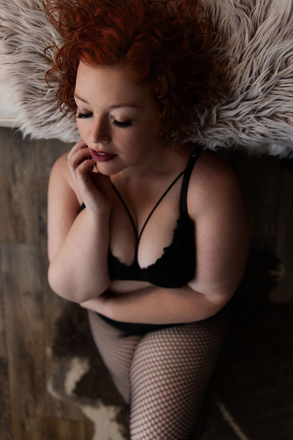 Woman with tattoos posing in black lingerie with finger near lips, intimate boudoir portrait