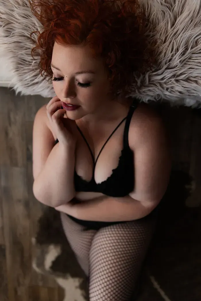 Woman with red curly hair lying on a fur blanket in black lingerie, boudoir portrait Indianapolis