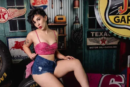 Pinup photography Indianapolis: woman in a retro pink top and denim shorts on a vintage garage set