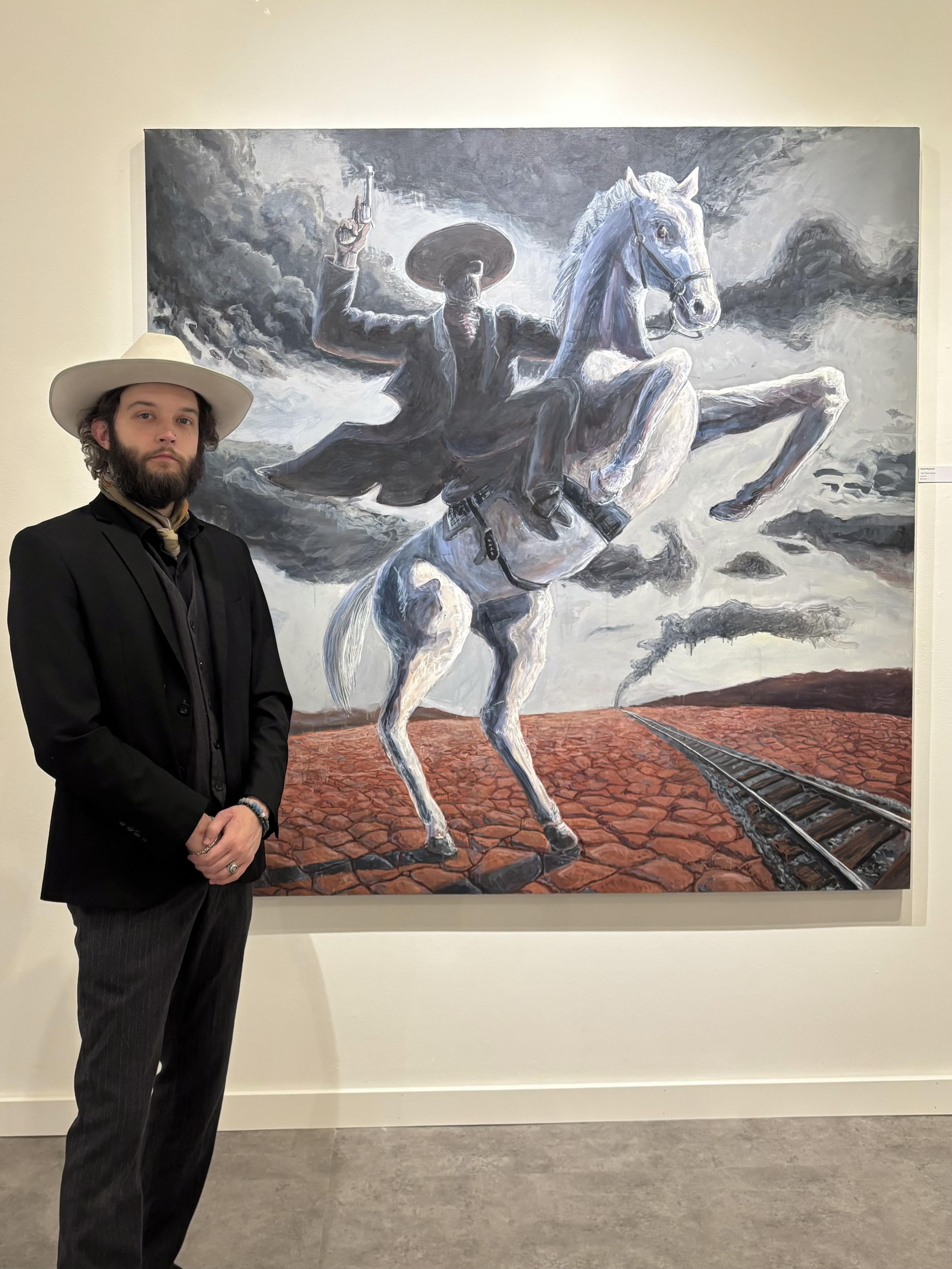 David Reynaud in font of one of his paintings of a cowboy riding a pale white horse.
