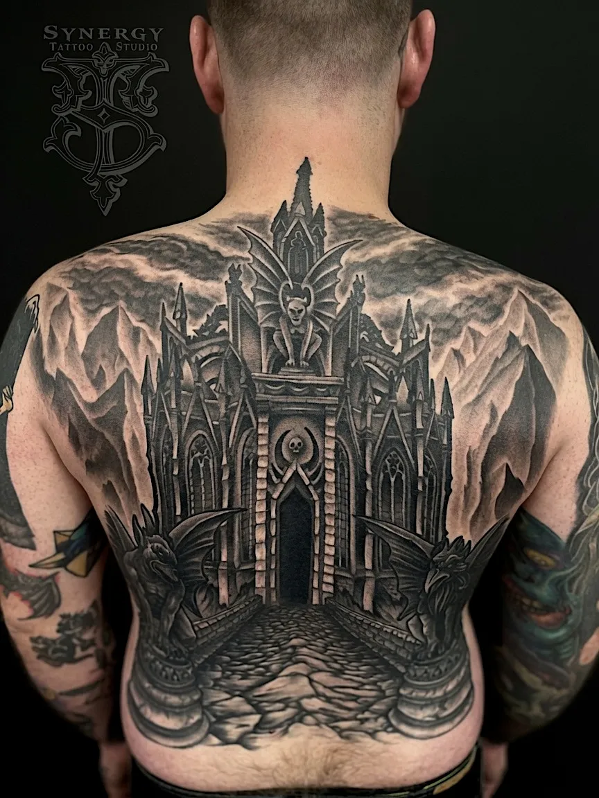 Black and grey full-back tattoo of a gothic cathedral beneath mountains