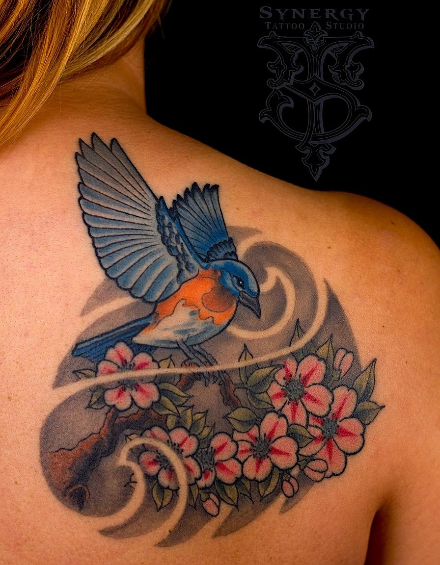 Blue and orange bird tattoo with pink blossoms and flowing waves