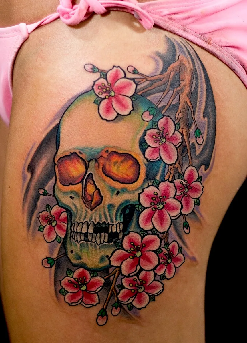 Skull and pink blossom tattoo on the upper thigh