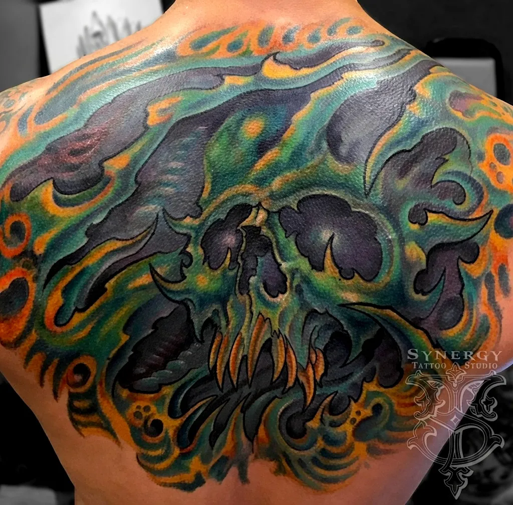 Green and orange skull tattoo with flowing organic shapes across the shoulder