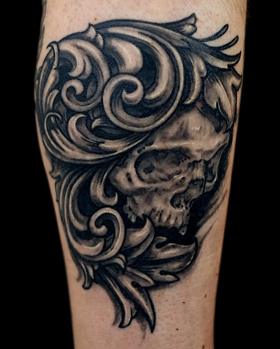 Black and grey skull tattoo framed by bold ornamental scrollwork
