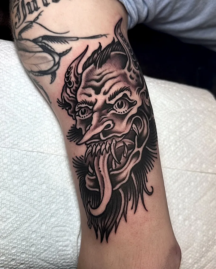 Black and grey long-tongued demon mask tattoo