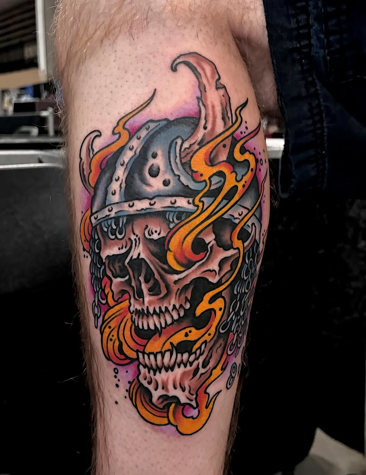 Color skull tattoo wearing a helmet and surrounded by orange flames