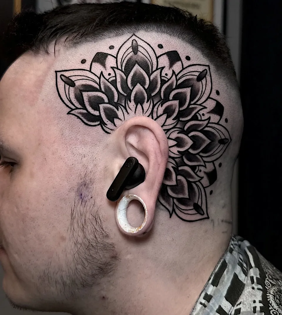 Black ornamental mandala tattoo extending around the ear