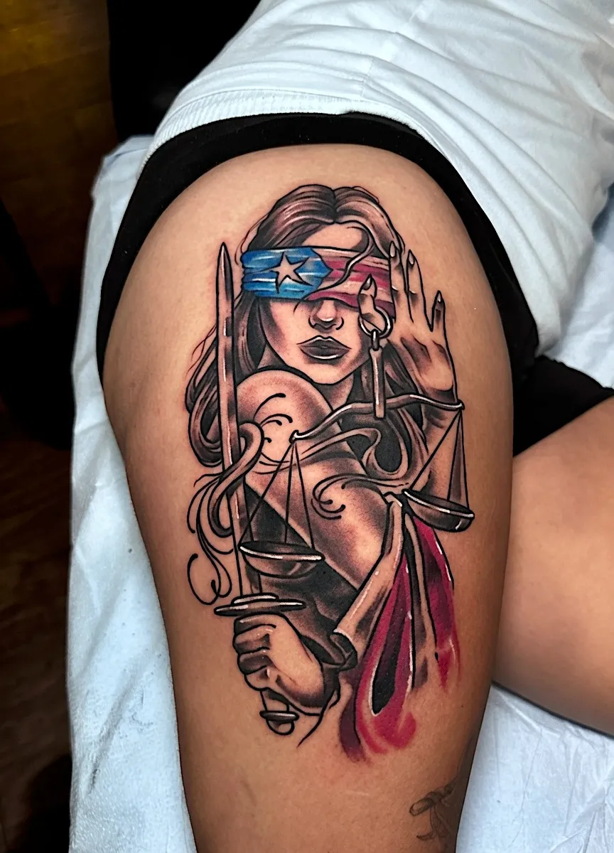 Lady Justice tattoo with scales, a sword, and a Puerto Rican flag blindfold