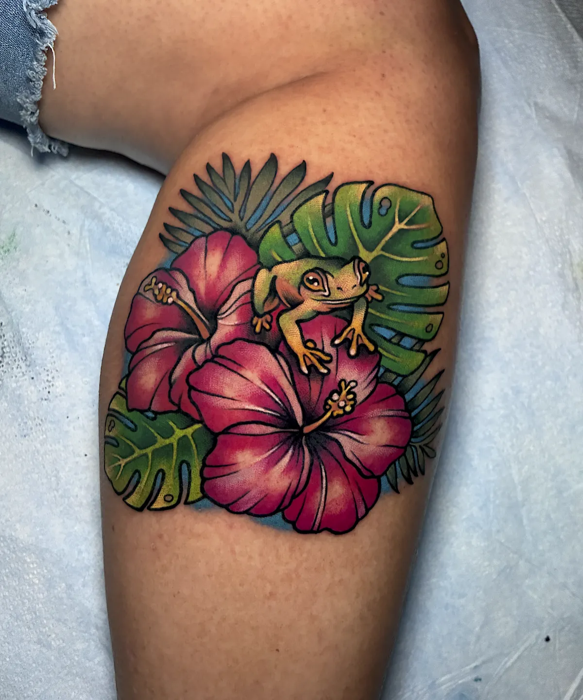 Tropical tattoo with a yellow frog, pink hibiscus flowers, and green monstera leaves