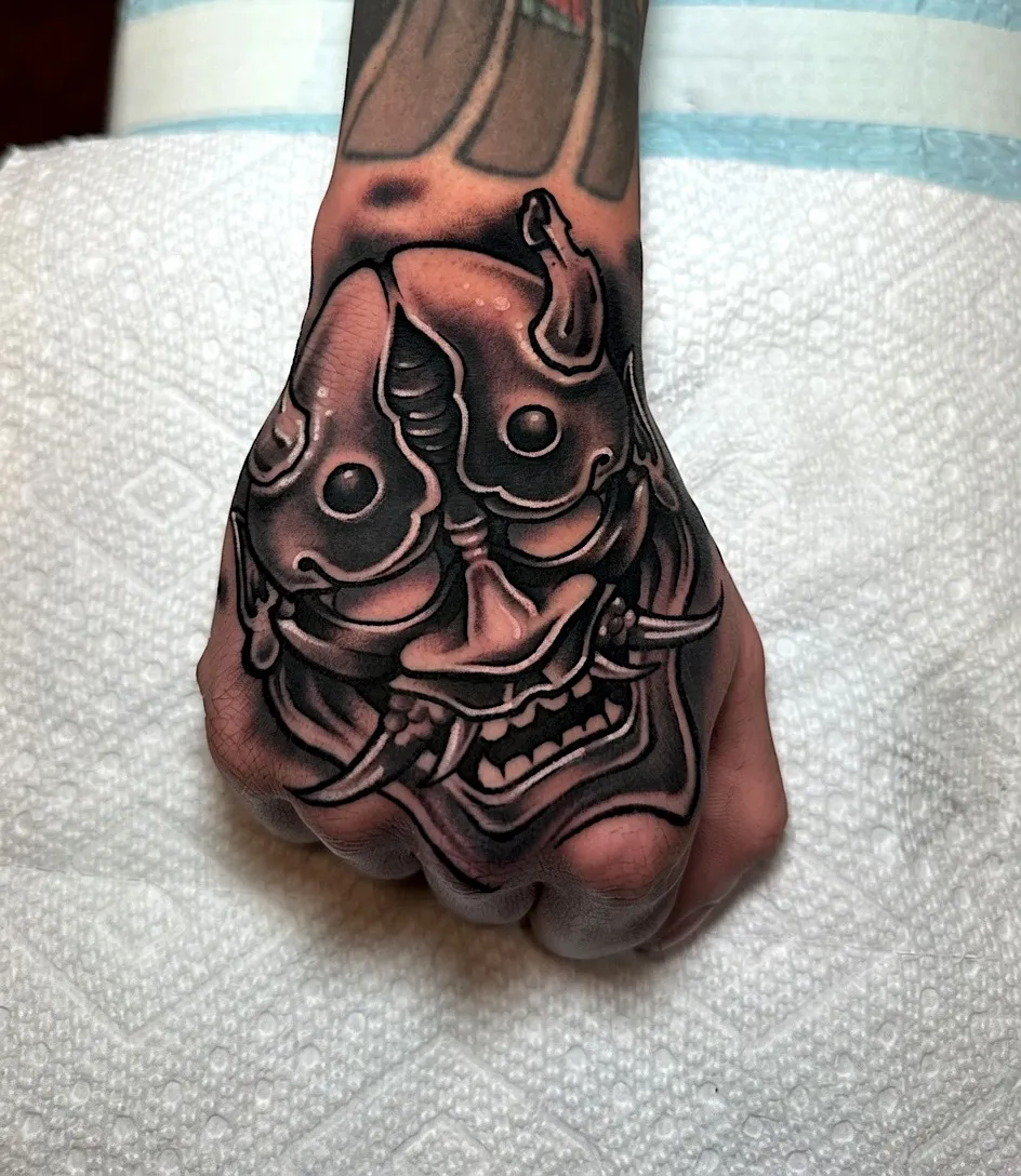 Black and grey Japanese demon mask tattoo on the back of the hand