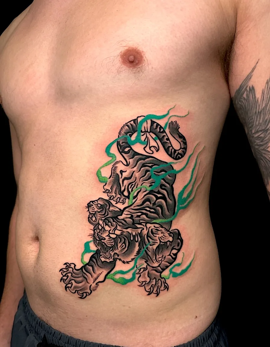 Tiger tattoo with a curled tail and green swirling background on the ribs
