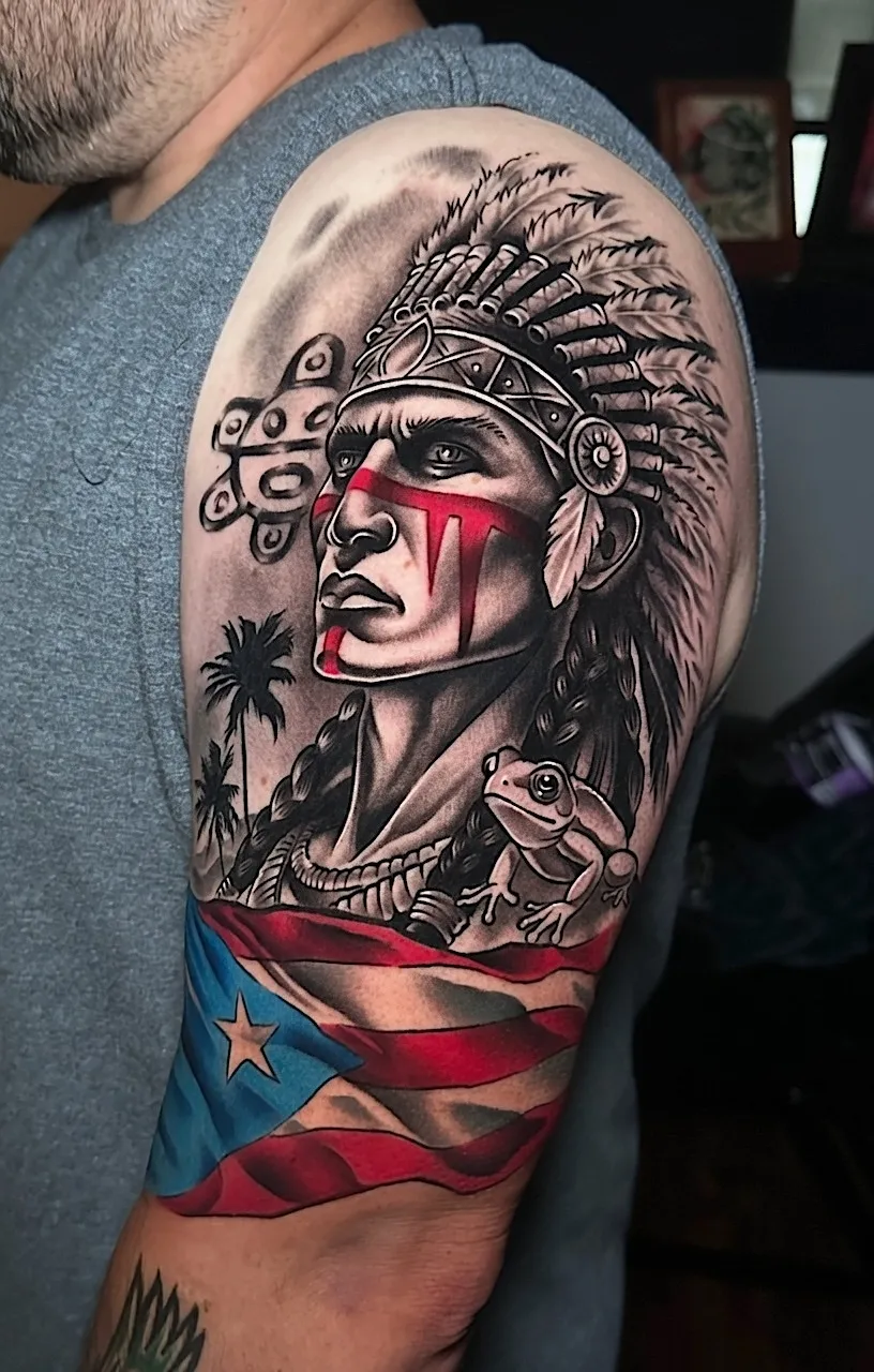 Upper-arm tattoo featuring a feathered portrait, coqui frog, and Puerto Rican flag