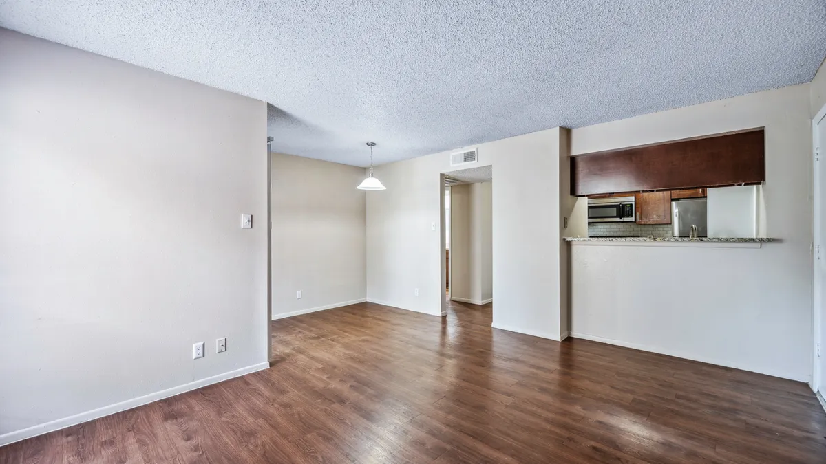Spacious open-concept apartment living room with wood-style flooring and a view into the kitchen pass-through at Winston Apartments in San Antonio.