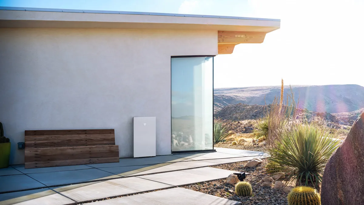 A Tesla Powerwall 3 on the outside wall of a home with a patio bench and desert landscaping