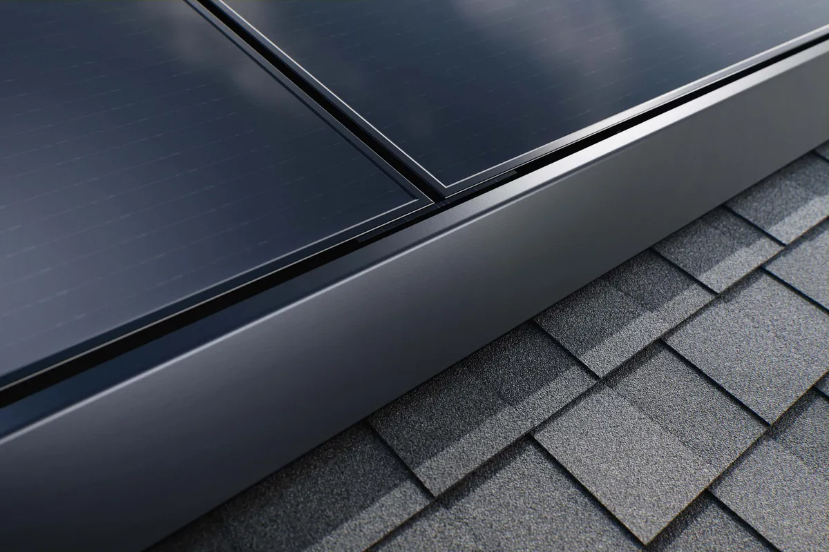 Close-up of the low-profile edge of black solar panels above asphalt roof shingles